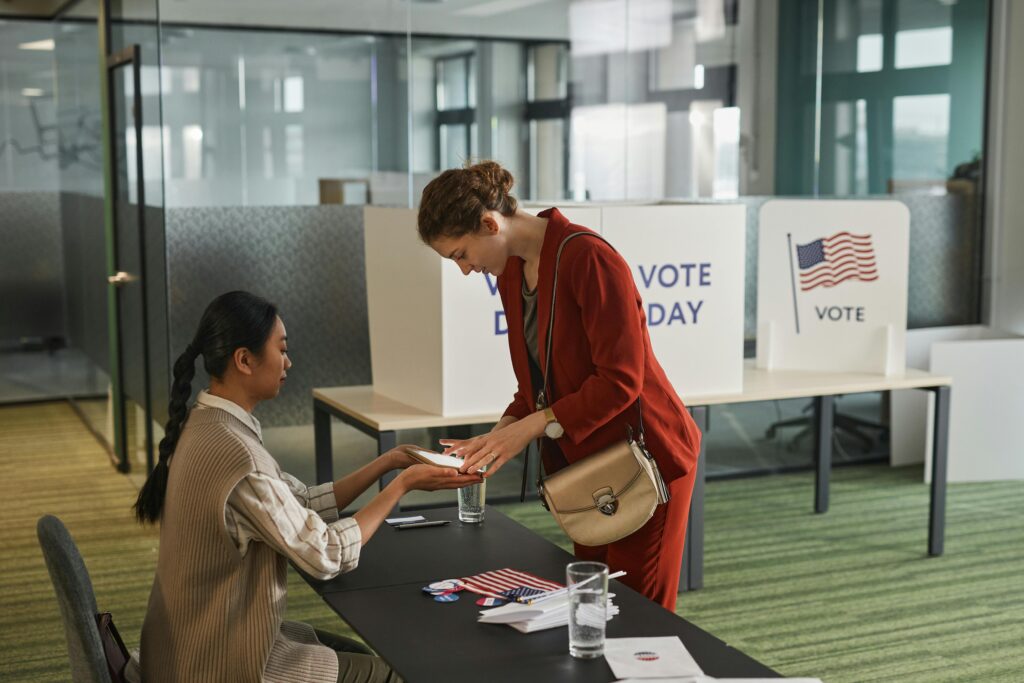 Two women interacting at a registration desk on election day indoors.